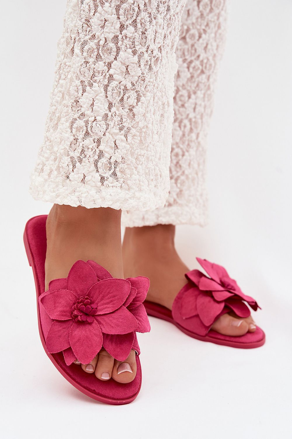 Pink sandals with floral design worn with a white lace dress on a white background