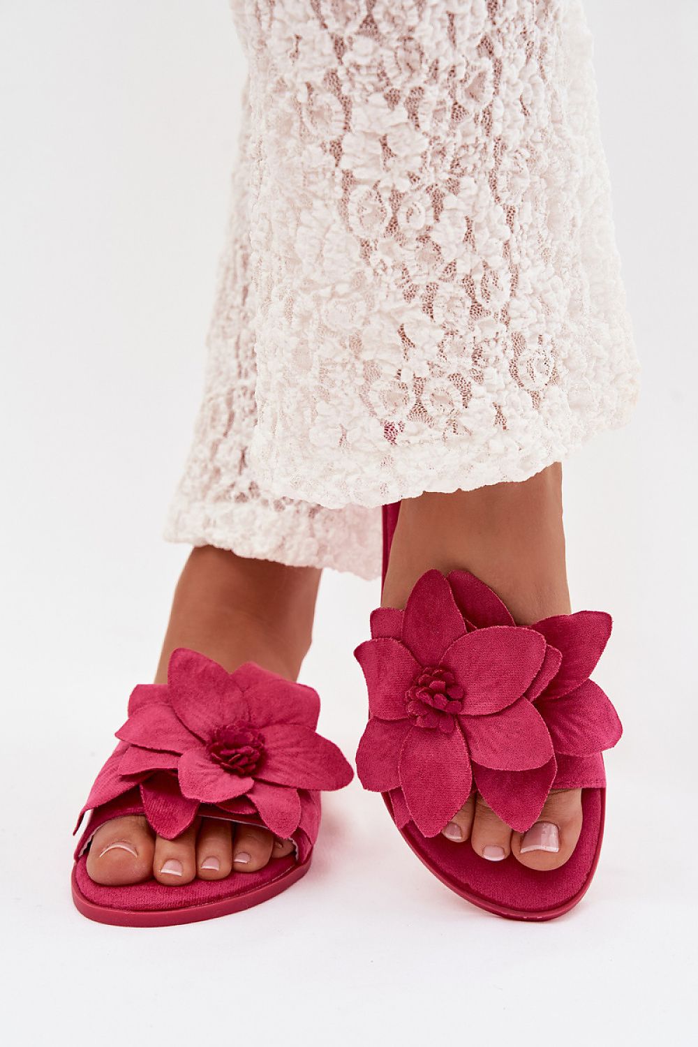 Pink floral sandals worn with a white lace dress on a white background