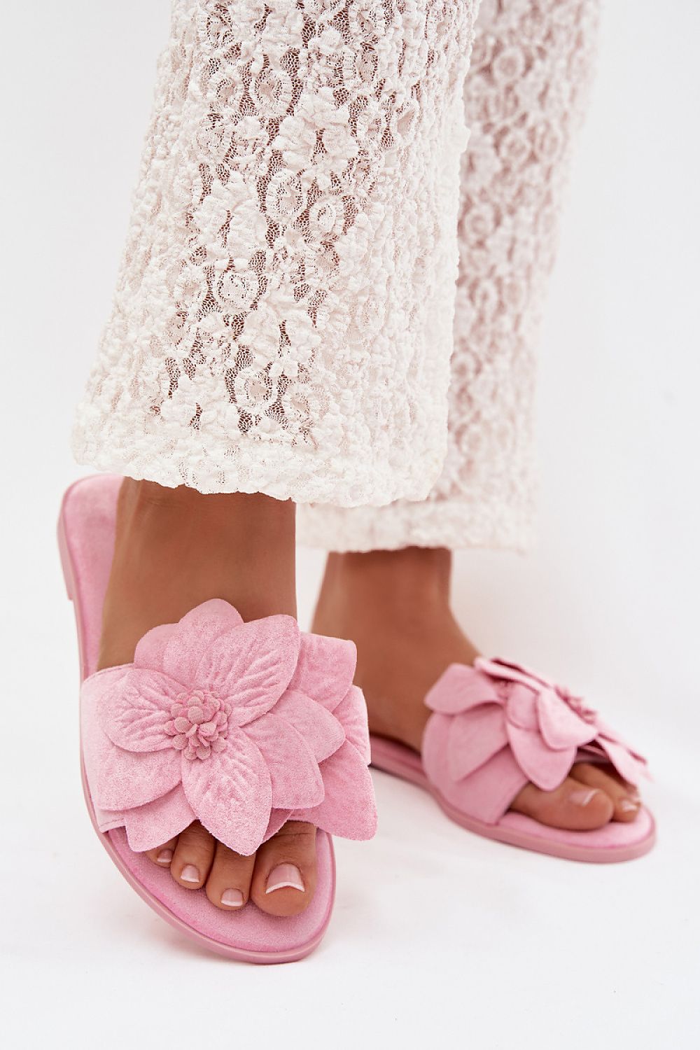Pink sandals with floral design worn with a lace dress on a white background