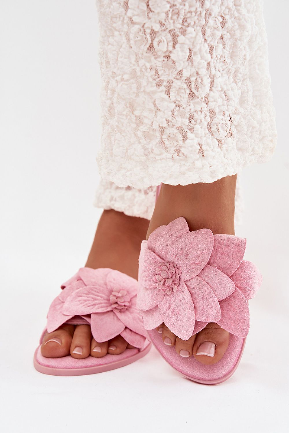 Pink sandals with large floral designs worn by a person in a white lace dress.
