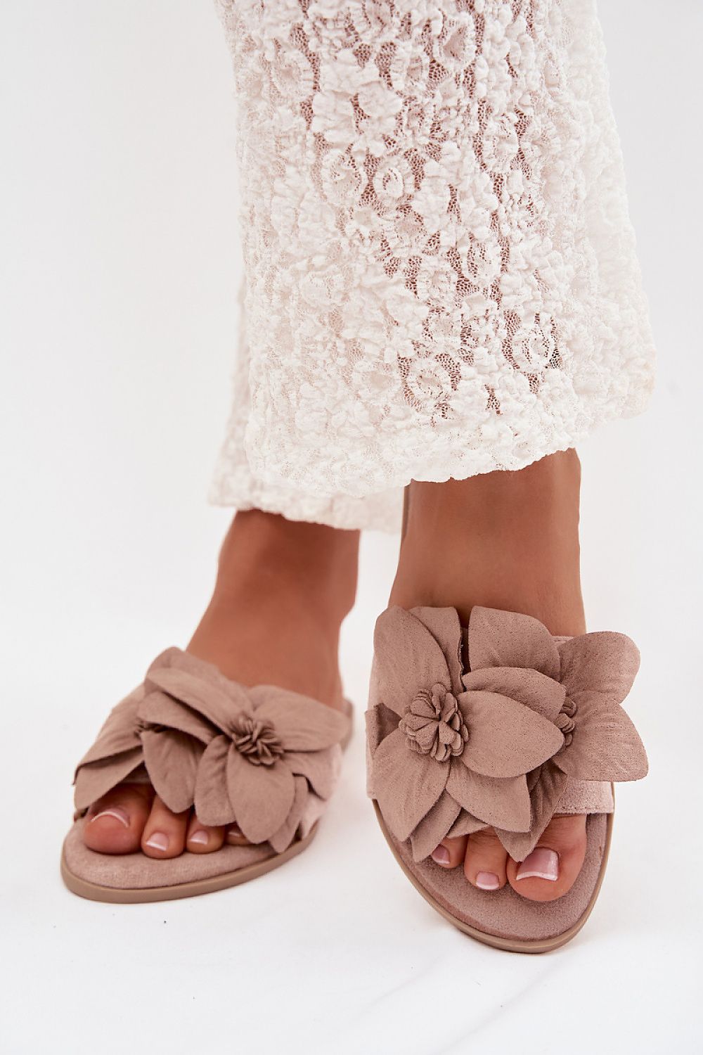 Brown sandals with floral details worn with a lace dress on a white background