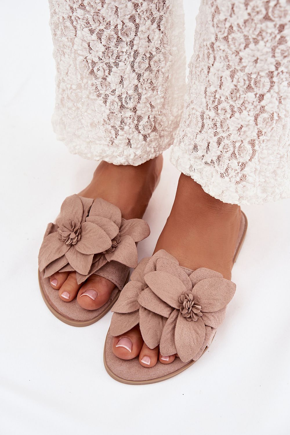 Beige sandals with floral decorations worn with white lace pants on a white background