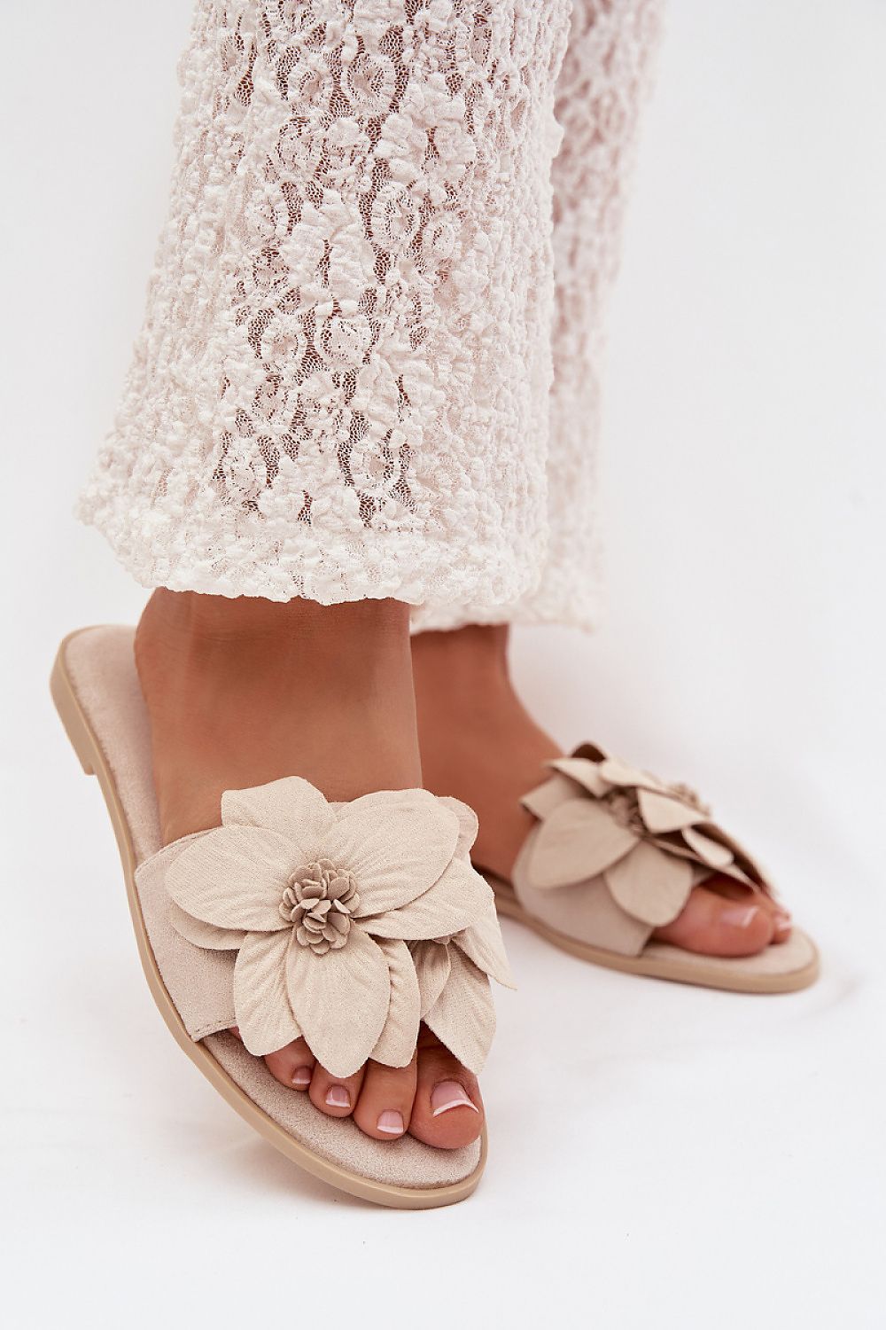 Beige sandals with floral design worn by a person in a white lace outfit on a light background