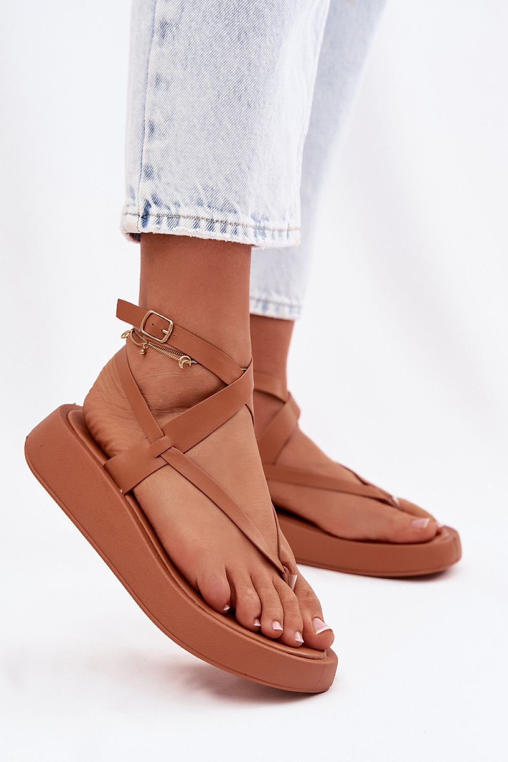 Brown sandals worn with light blue jeans on a white background