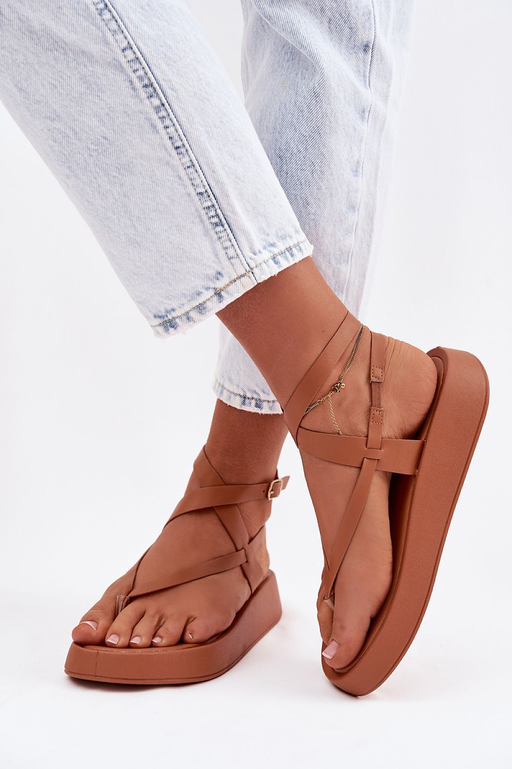 Brown sandals worn with light blue jeans on a white background