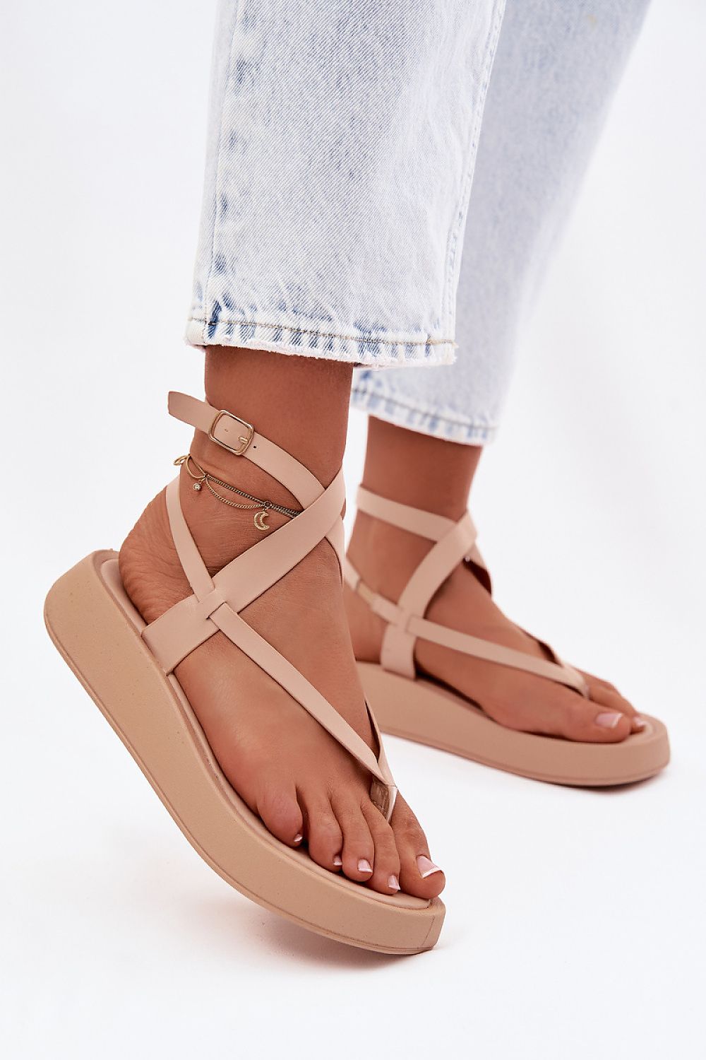 Beige sandals worn with light blue jeans on a white background