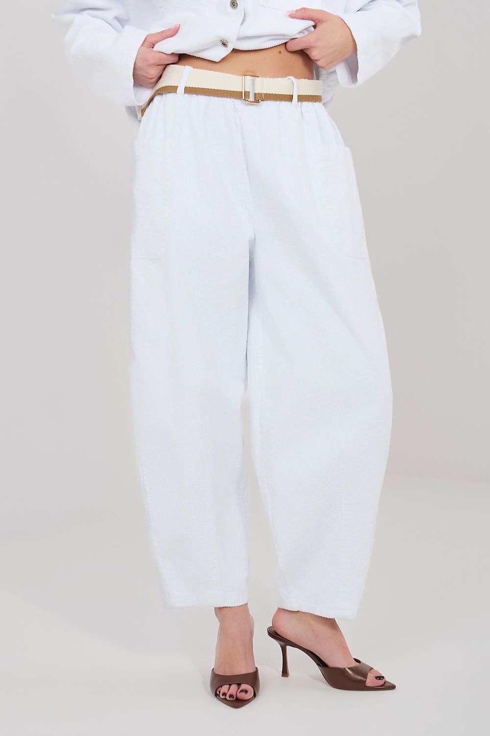 Person wearing white pants with a beige belt on a plain background