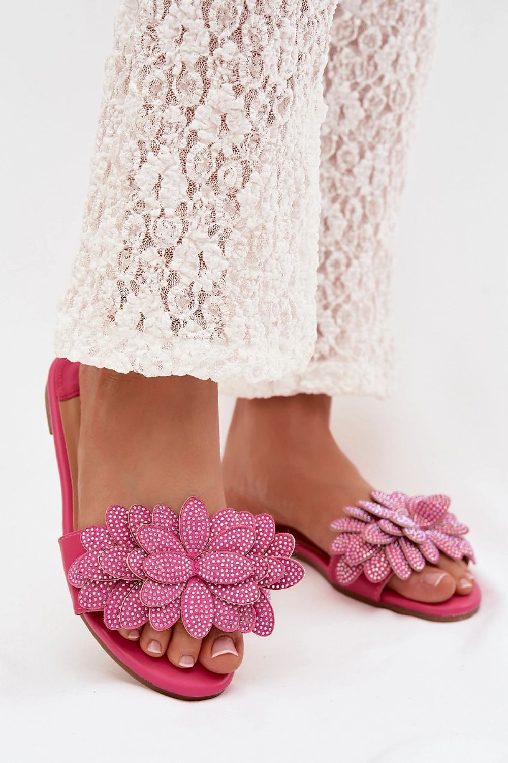 Pink sandals with floral embellishments worn with a white lace skirt on a white background
