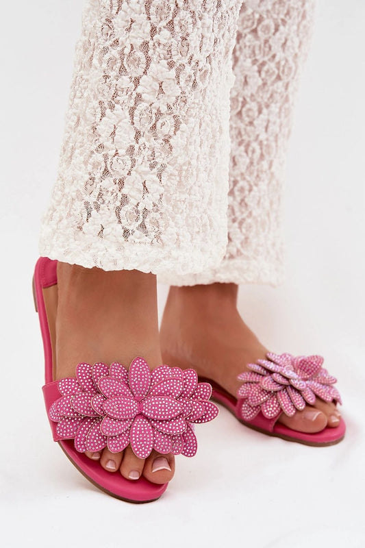 Pink sandals with floral embellishments worn with a white lace skirt on a white background