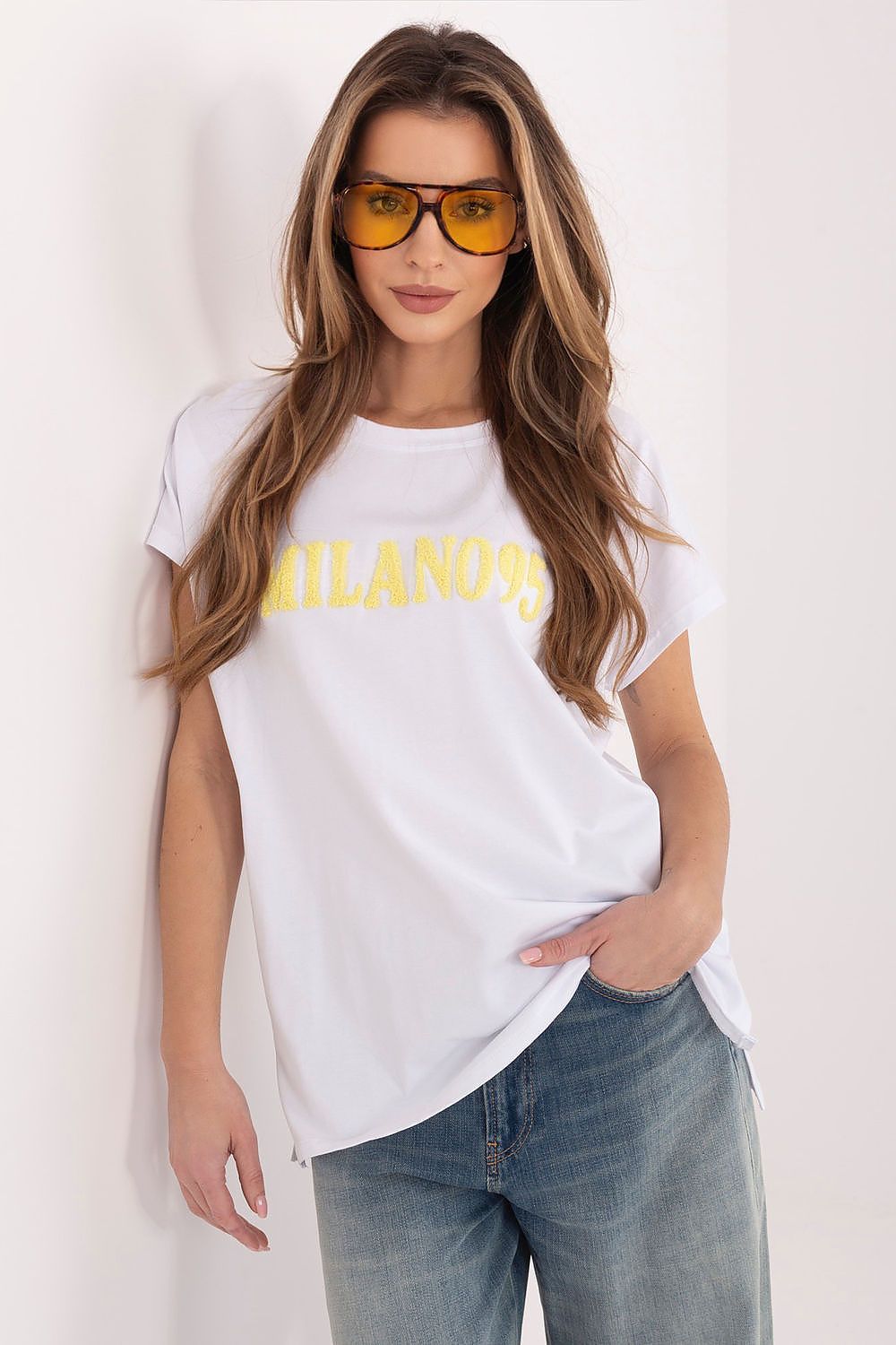 Woman wearing a white t-shirt with 'Milano' printed in yellow and sunglasses on a plain background