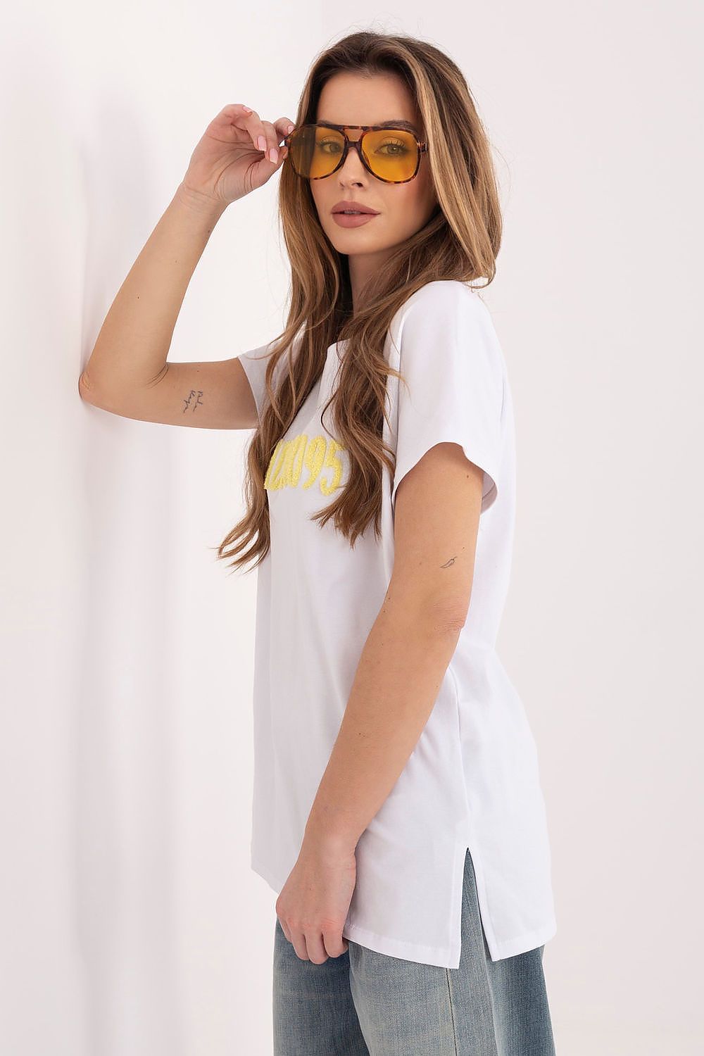 Woman wearing a white t-shirt with a yellow graphic and sunglasses on a plain background