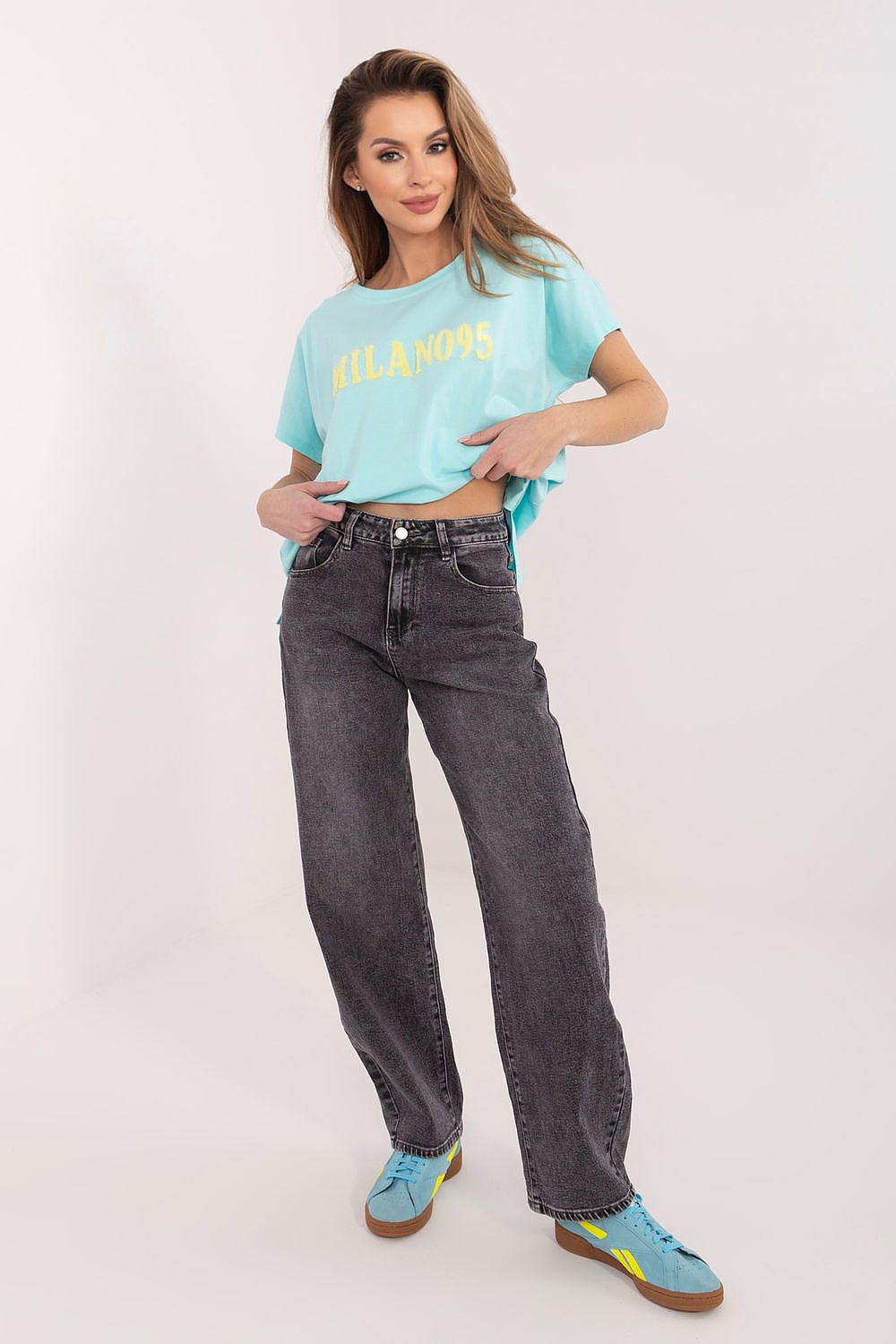 Woman wearing a light blue t-shirt with text and dark jeans on a white background