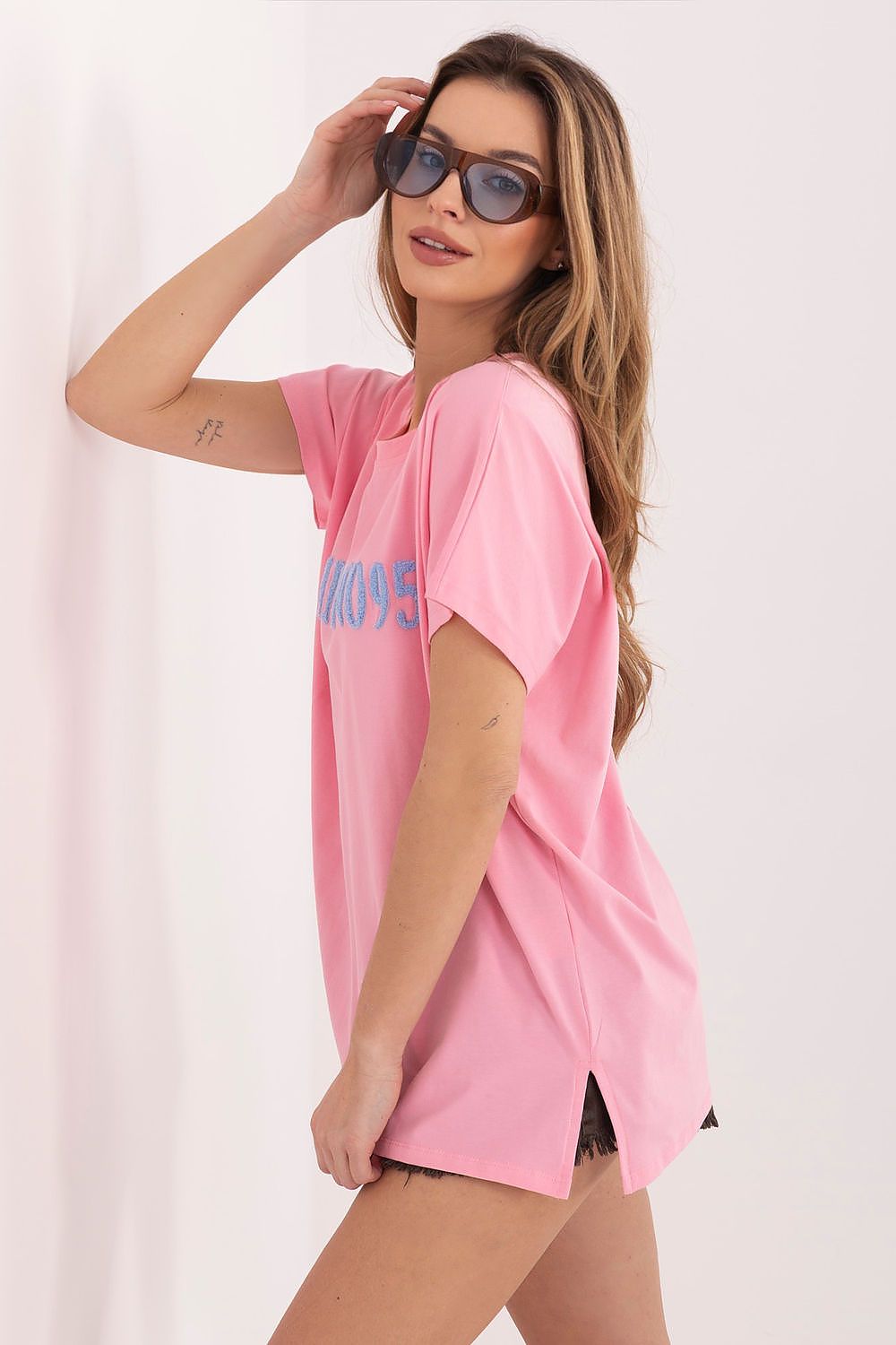 Woman wearing a pink oversized t-shirt with text on a plain background