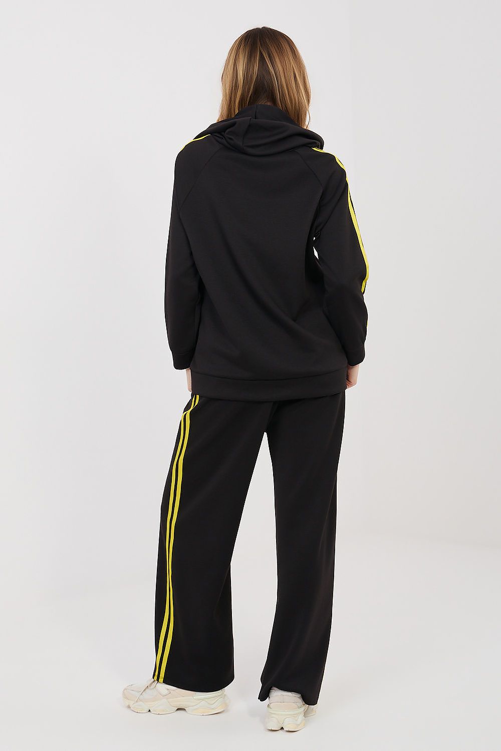 Person wearing a black tracksuit with yellow stripes on a white background
