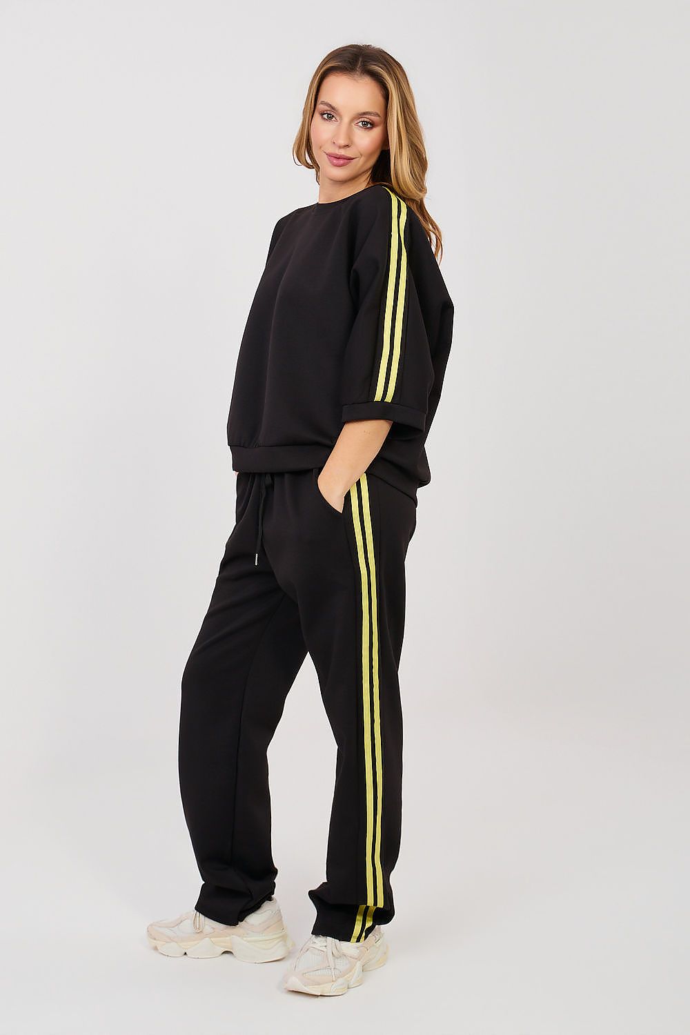 Woman wearing a black tracksuit with yellow stripes on a white background