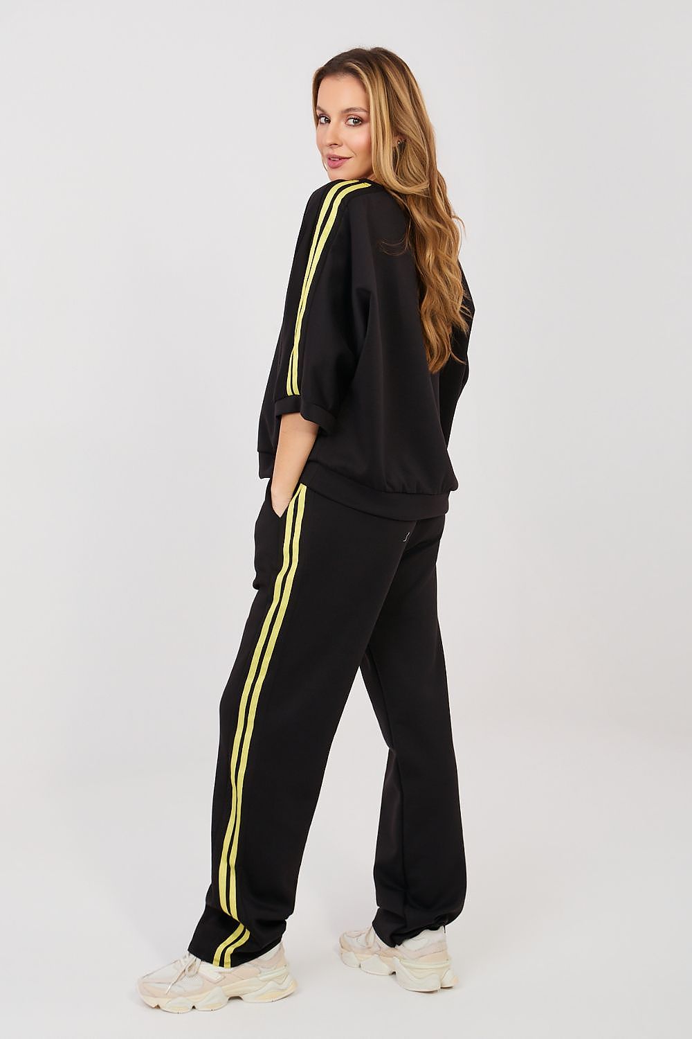 Woman wearing a black tracksuit with yellow stripes on a white background