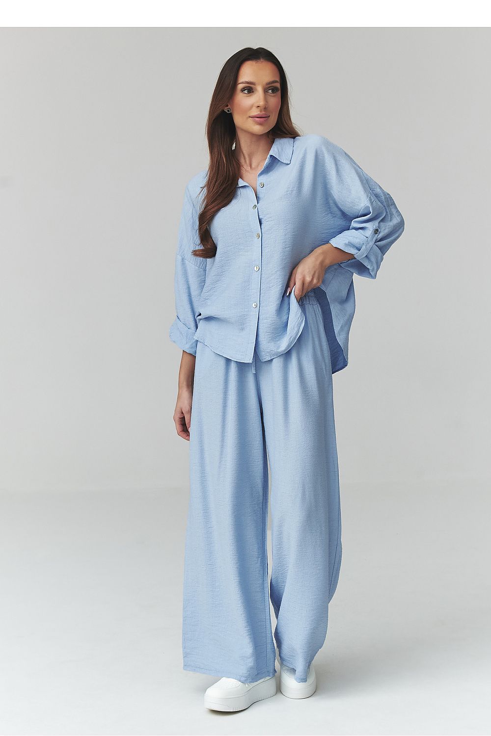 Woman wearing a light blue outfit with a shirt and wide-leg pants on a plain background
