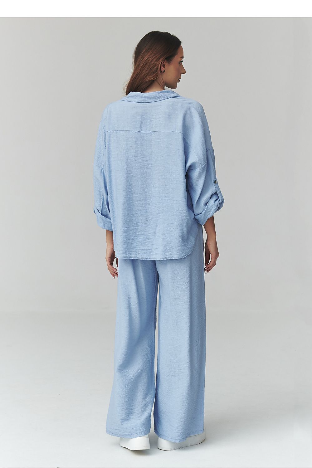 Woman wearing a light blue outfit with wide-leg pants on a plain background