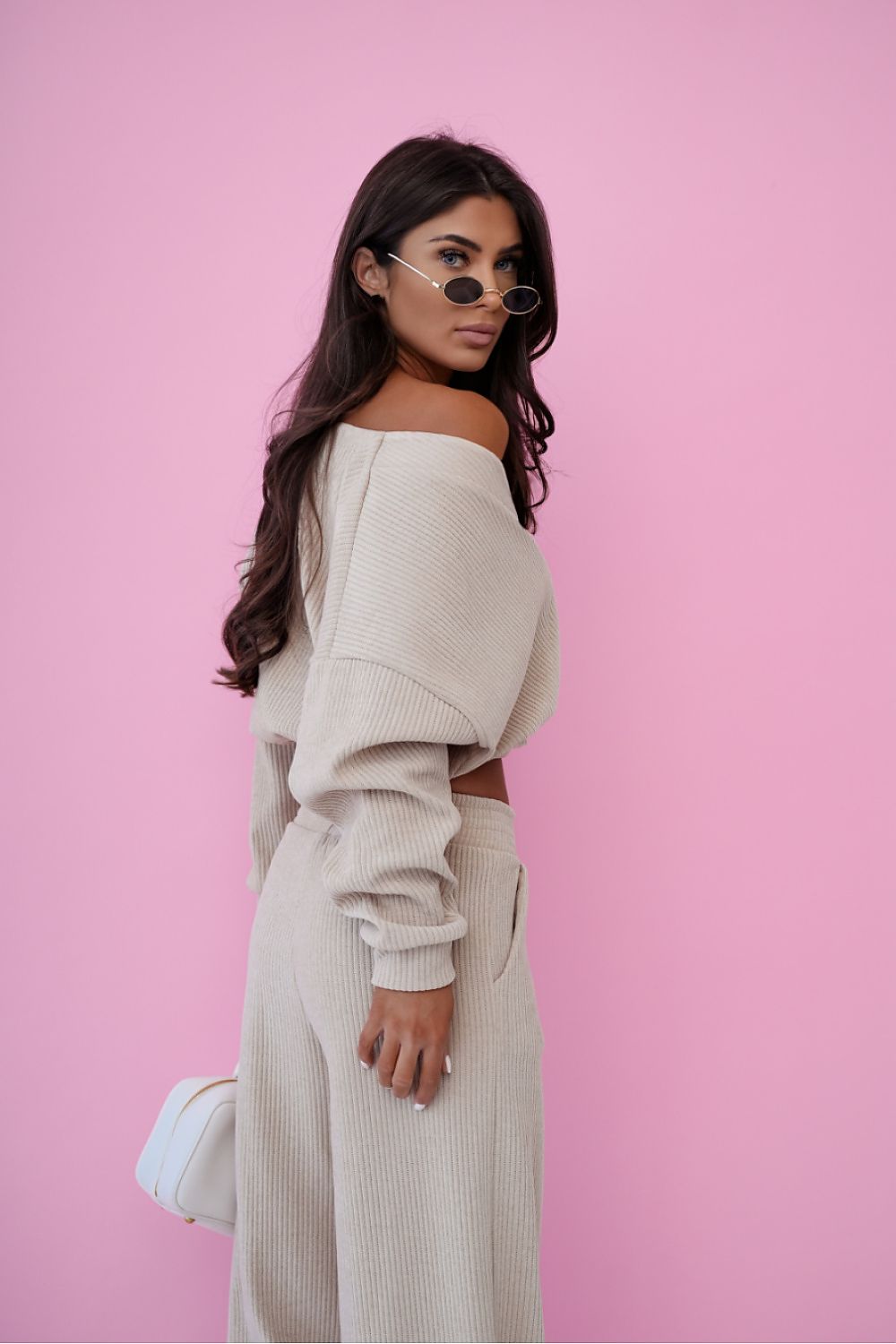 Woman wearing a beige off-shoulder top and pants against a pink background