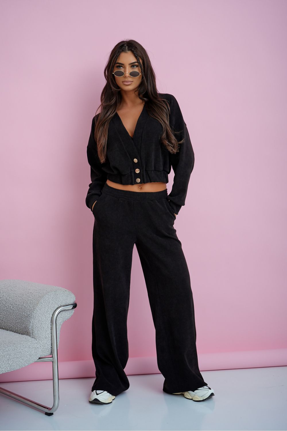 Woman in a black outfit standing against a pink wall