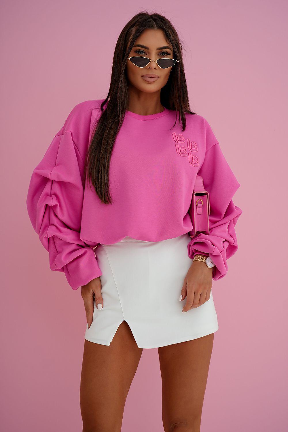 Woman wearing a pink sweatshirt and white skirt against a pink background