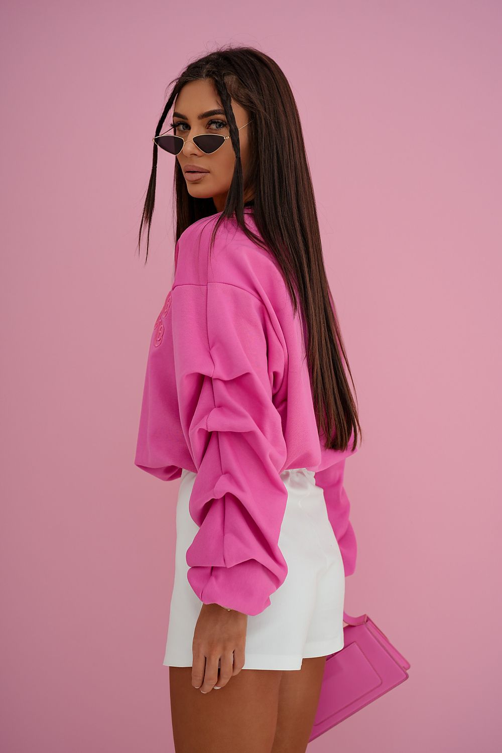 Woman wearing a pink sweatshirt and white shorts against a pink background