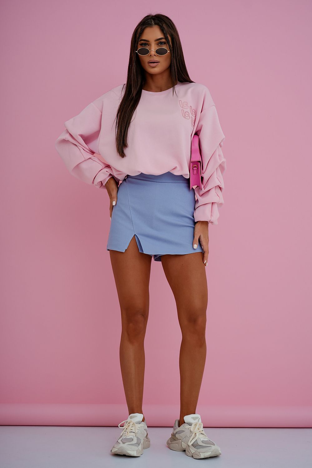 Woman wearing a pink sweatshirt and blue skirt against a pink background