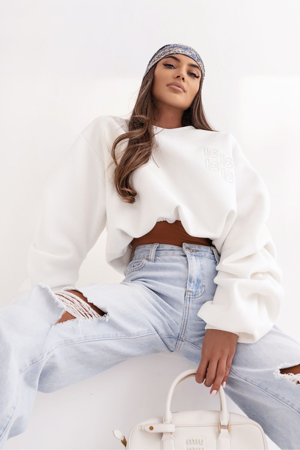 Woman wearing a white top and light blue jeans with a white handbag on a white background