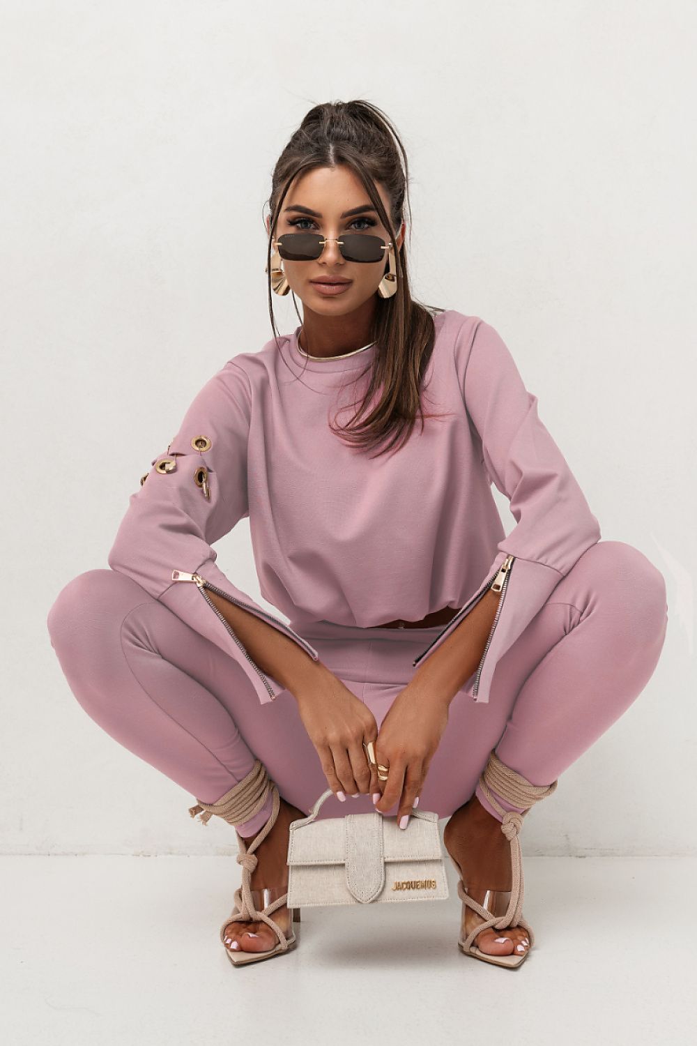 Woman in a pink outfit sitting on the floor with a white handbag.