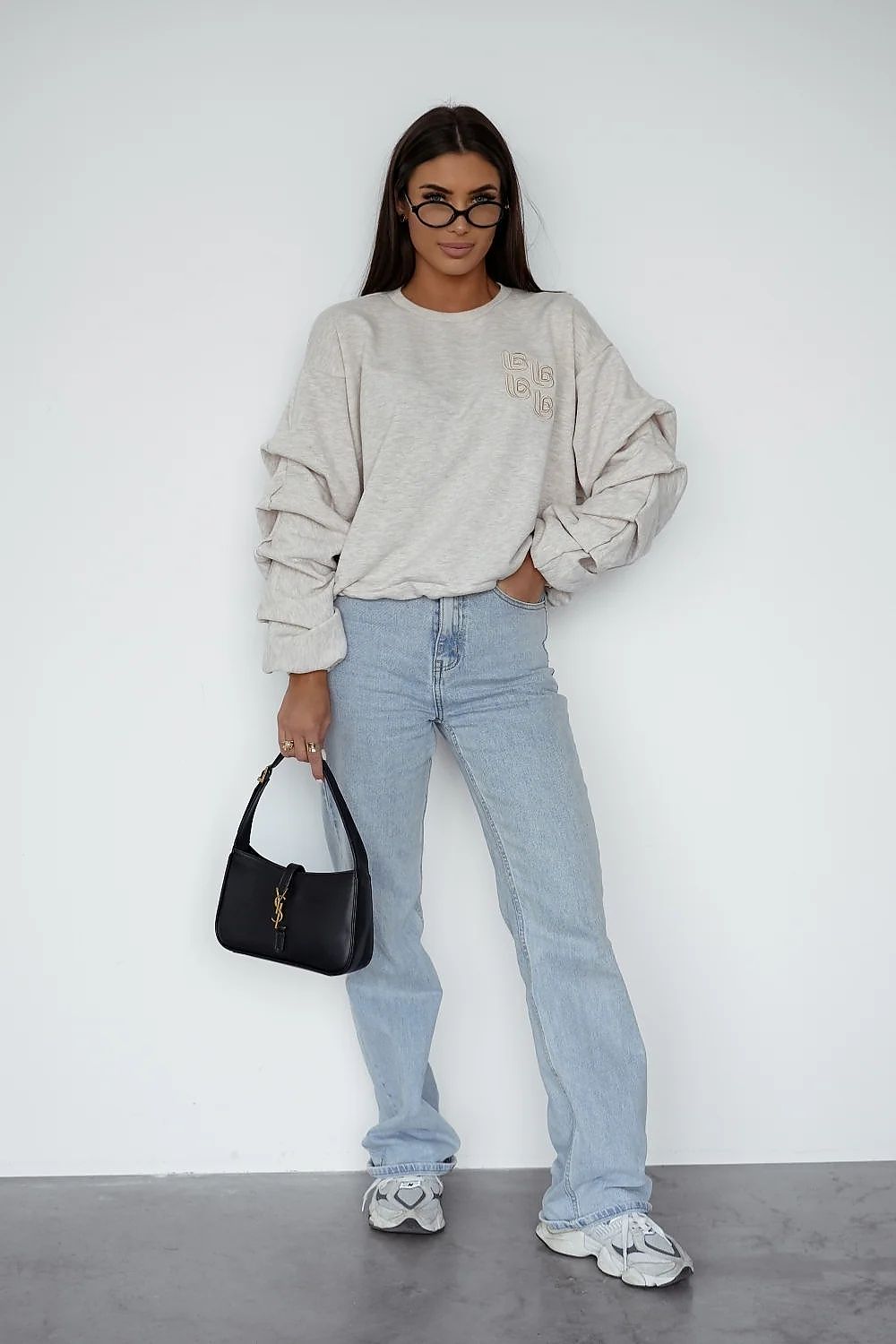 Person wearing a beige sweatshirt, light blue jeans, and white sneakers against a white background.