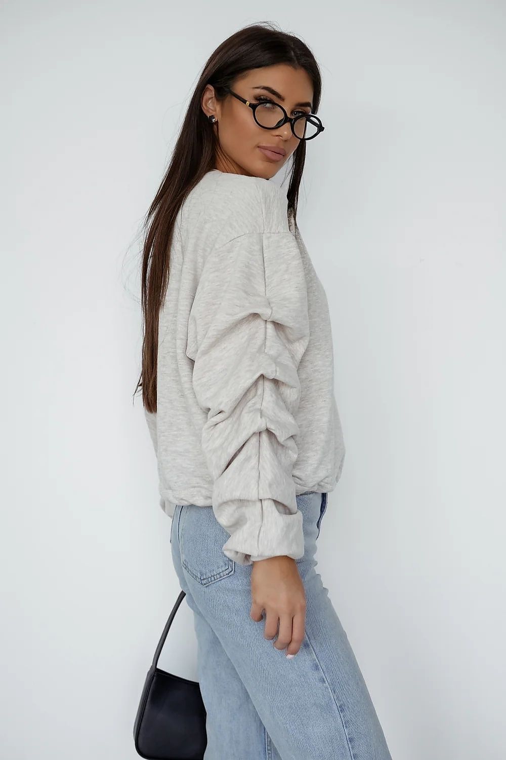 Woman wearing a light gray sweater and blue jeans against a white background