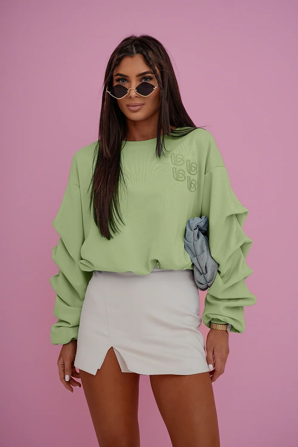 Woman wearing a light green sweater and white skirt against a pink background