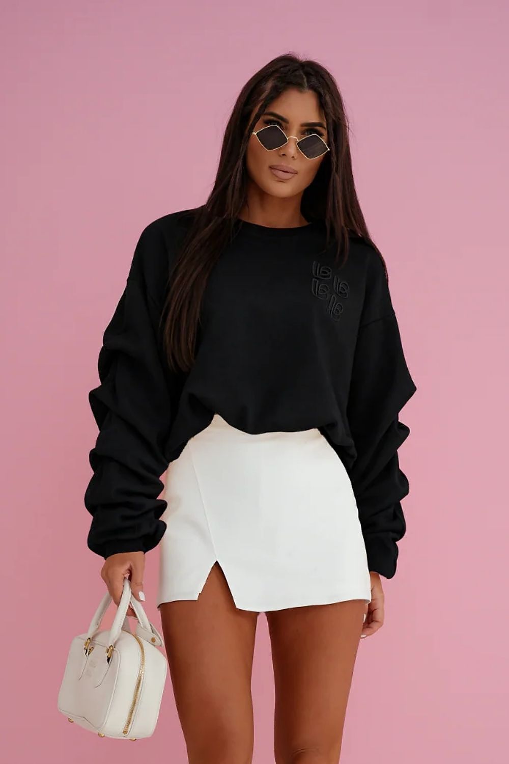 Woman wearing a black sweatshirt and white skirt against a pink background