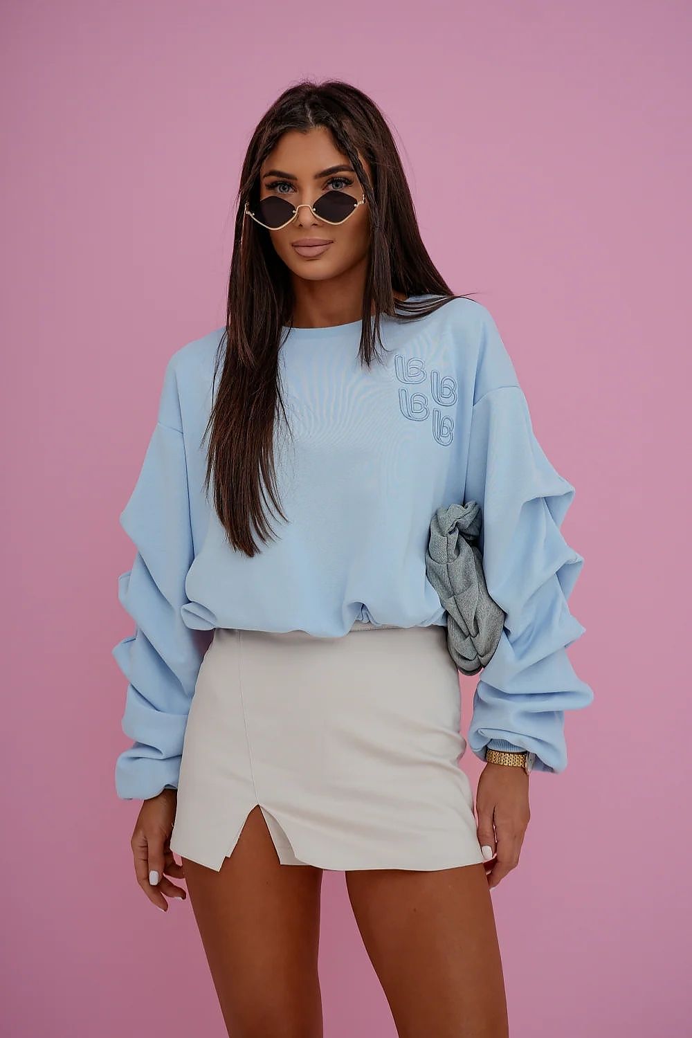 Woman wearing a light blue sweater and beige skirt against a pink background