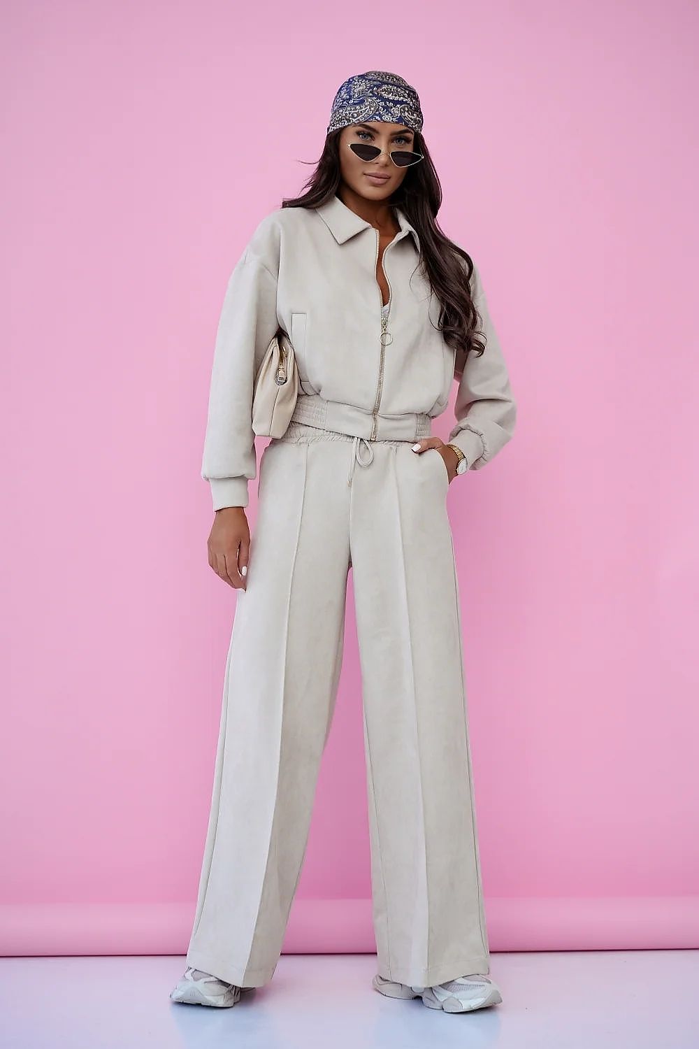 Woman in beige outfit with wide-leg pants against a pink background