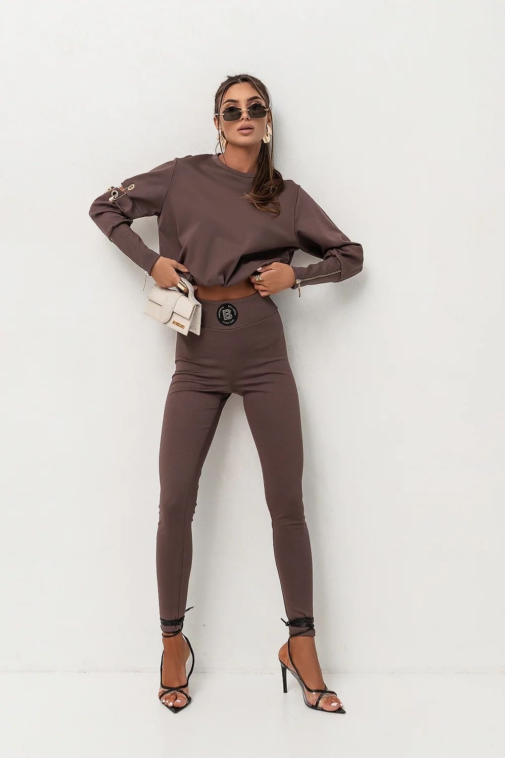 Woman wearing a brown outfit with sunglasses and a white bag on a white background