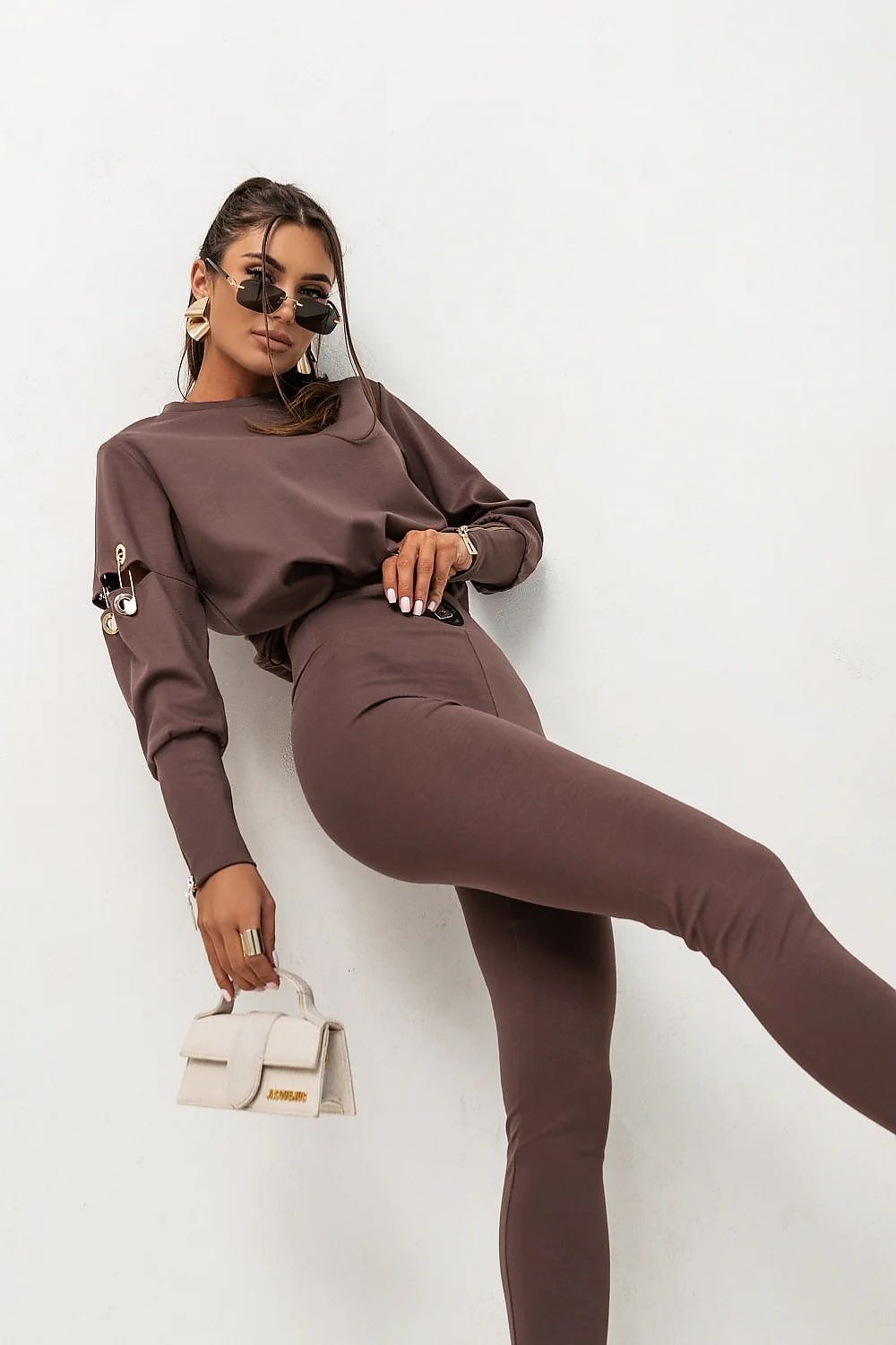 Woman in a brown outfit posing against a white wall