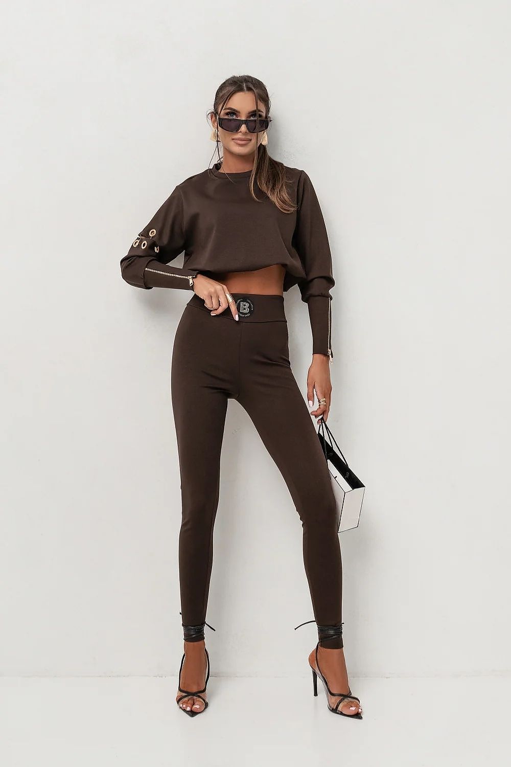 Woman wearing a brown outfit with a belt and high heels on a white background