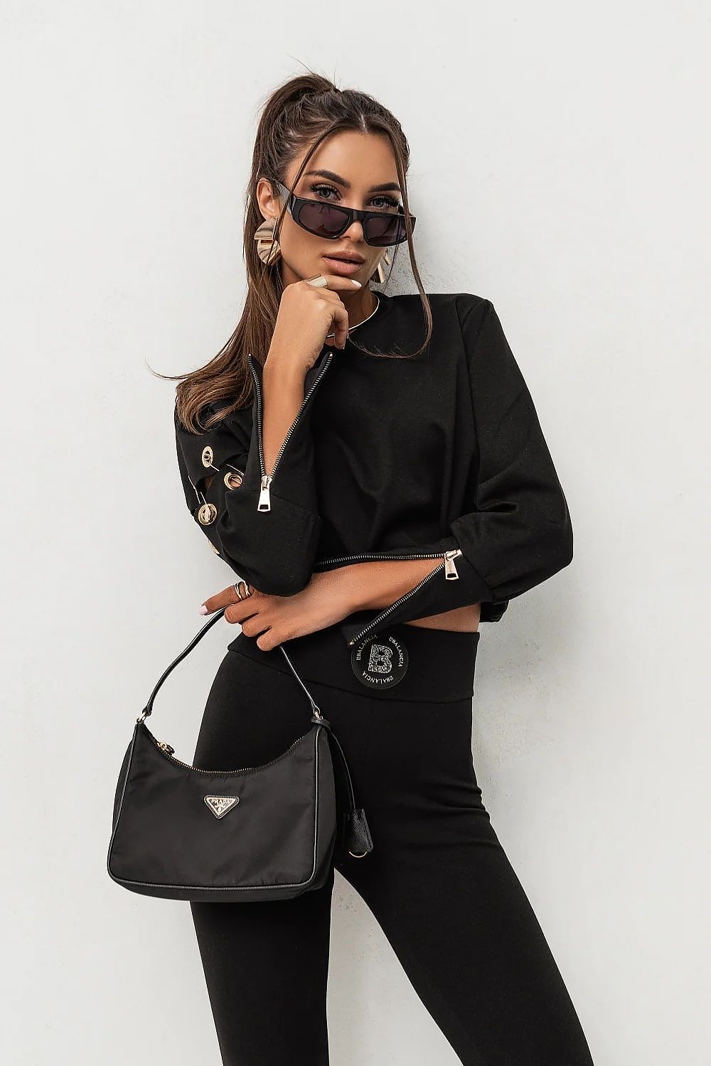 Woman in black outfit with sunglasses and a black handbag on a white background