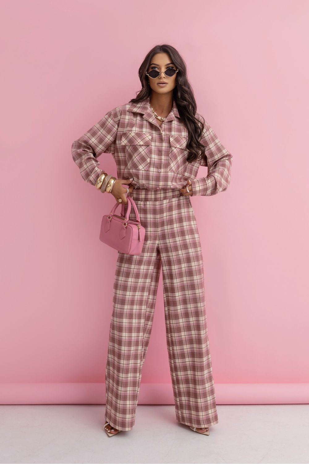 Woman in a pink plaid outfit holding a matching handbag against a pink background