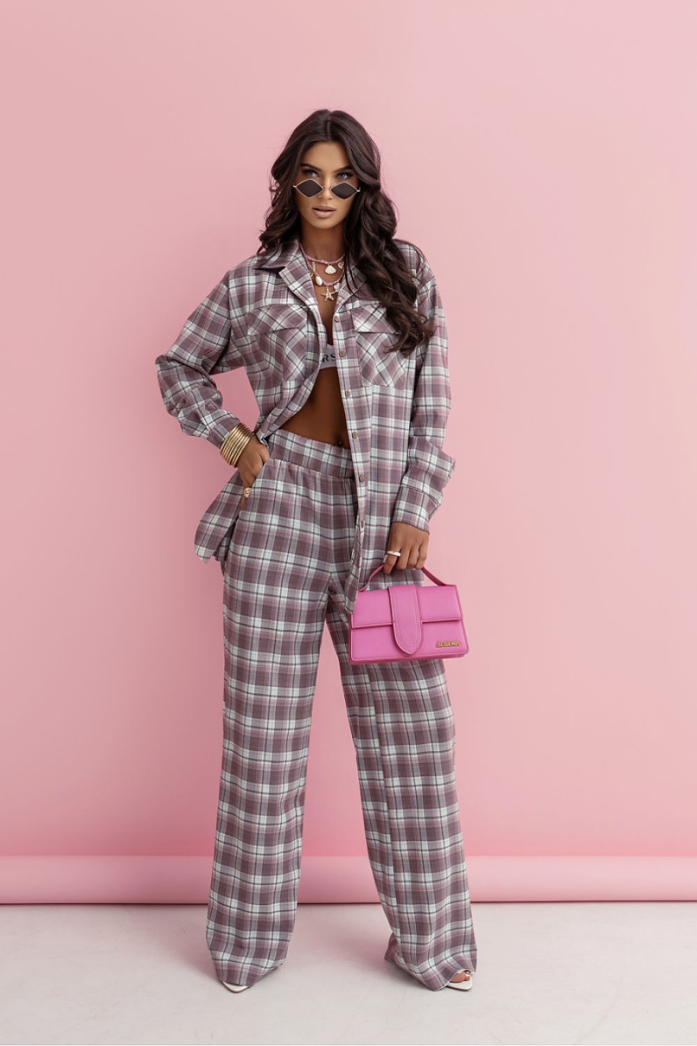 Woman in plaid outfit holding a pink handbag against a pink background