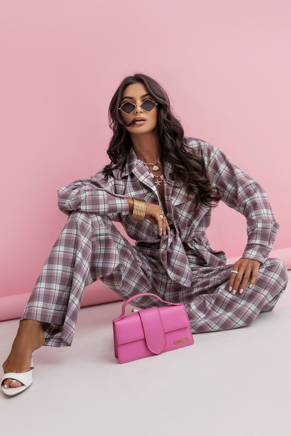 Woman in plaid outfit with pink handbag against a pink background