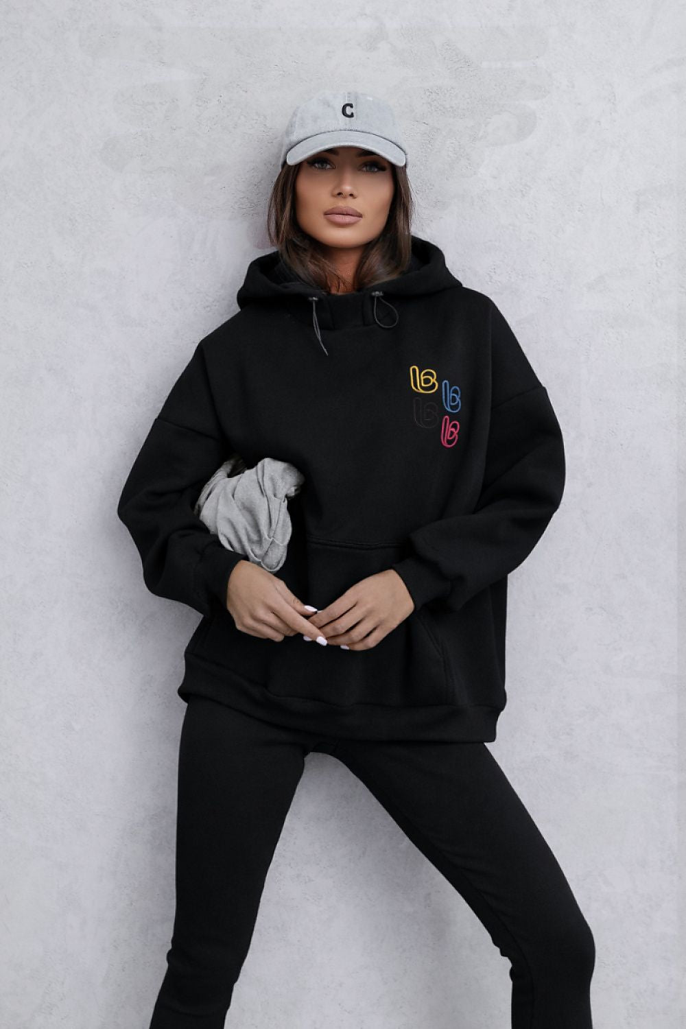 Person wearing a black hoodie with colorful patches on a light gray background