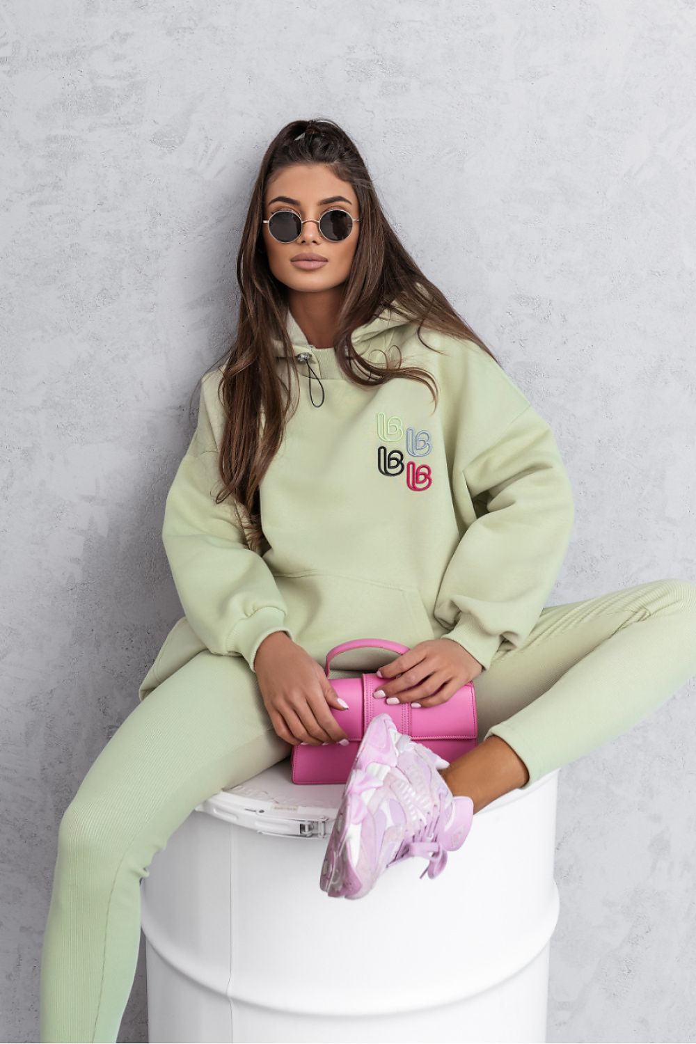 Person wearing a light green hoodie and pants sitting on a white toilet with a pink bag.