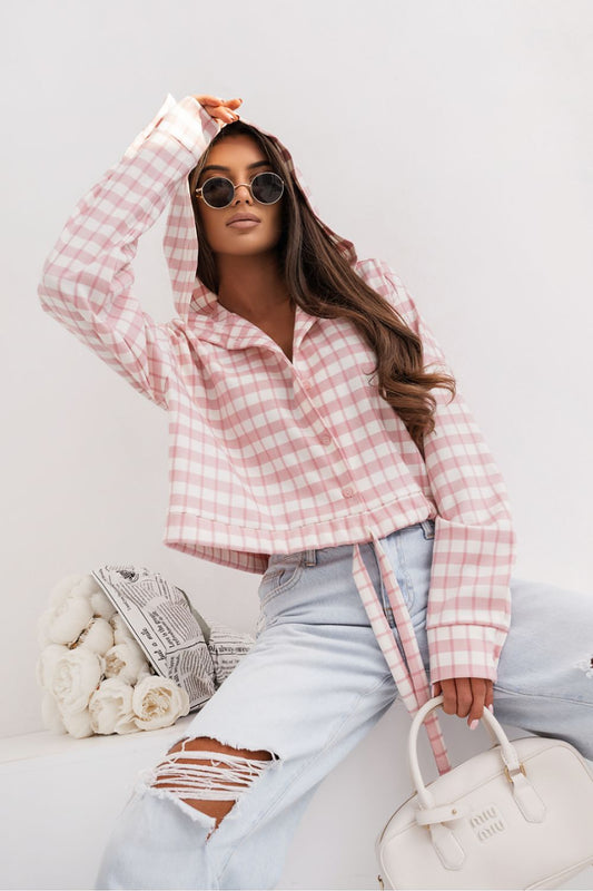 Woman wearing a pink plaid shirt and light blue jeans, sitting on a white surface with a white background.