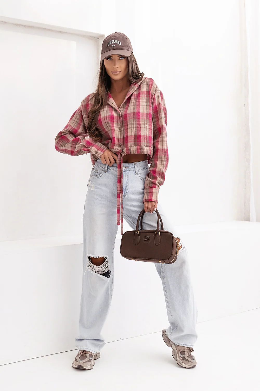 Person wearing a plaid shirt, light jeans, and a cap, holding a brown handbag on a white background