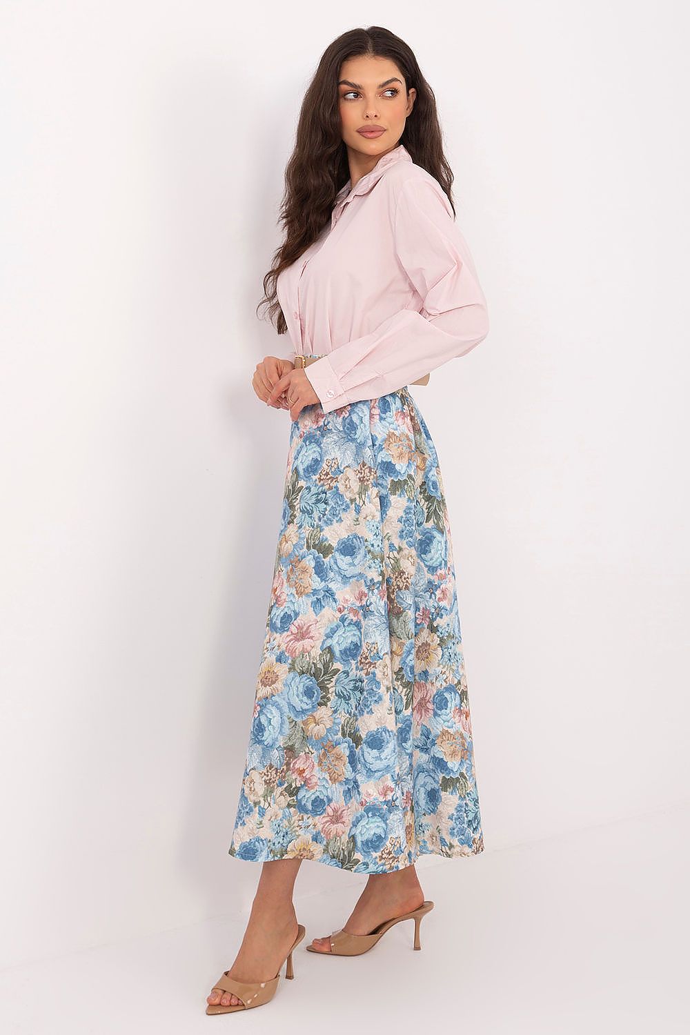 Woman wearing a light pink blouse and floral skirt against a white background