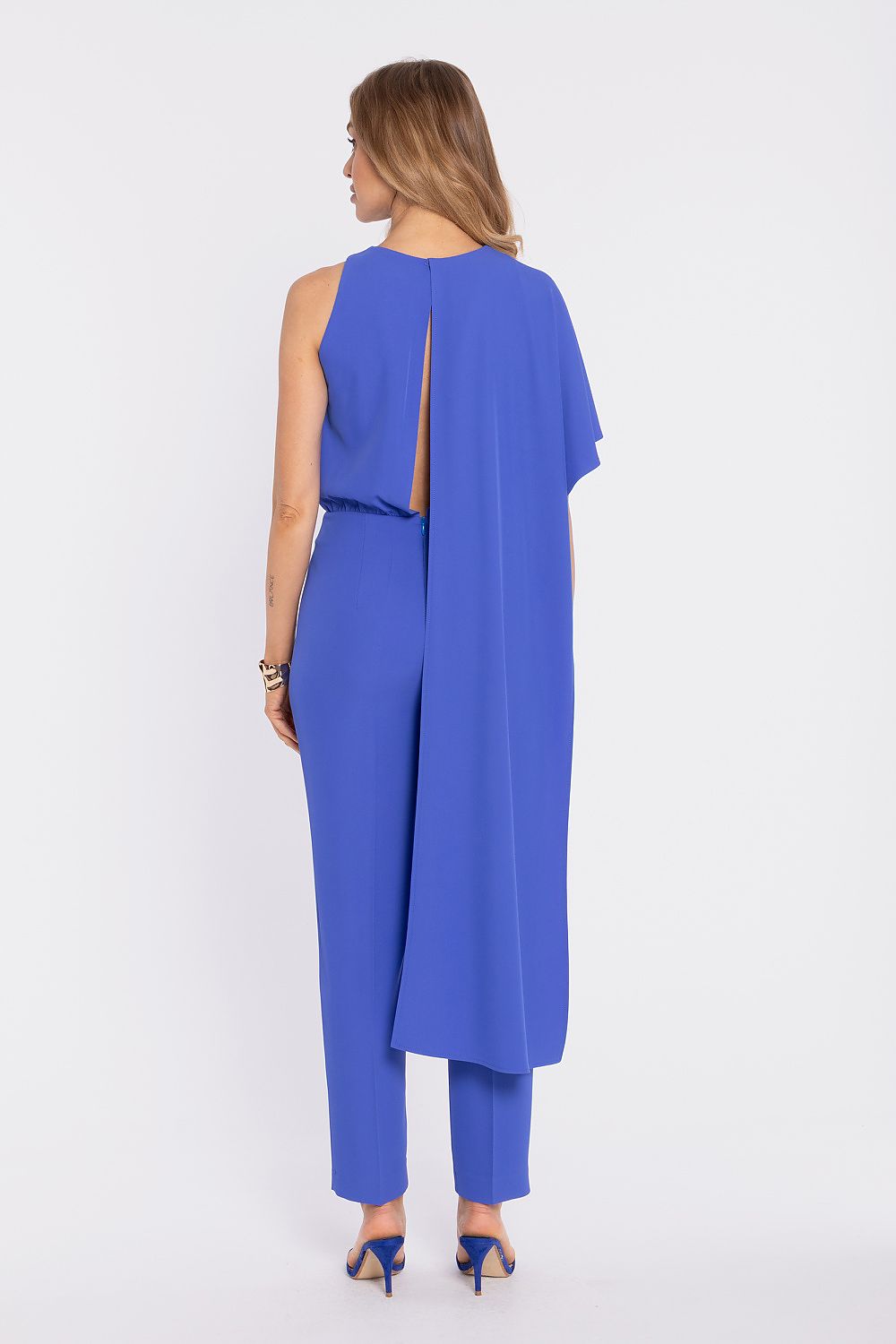 Woman wearing a blue jumpsuit with a slit back on a white background