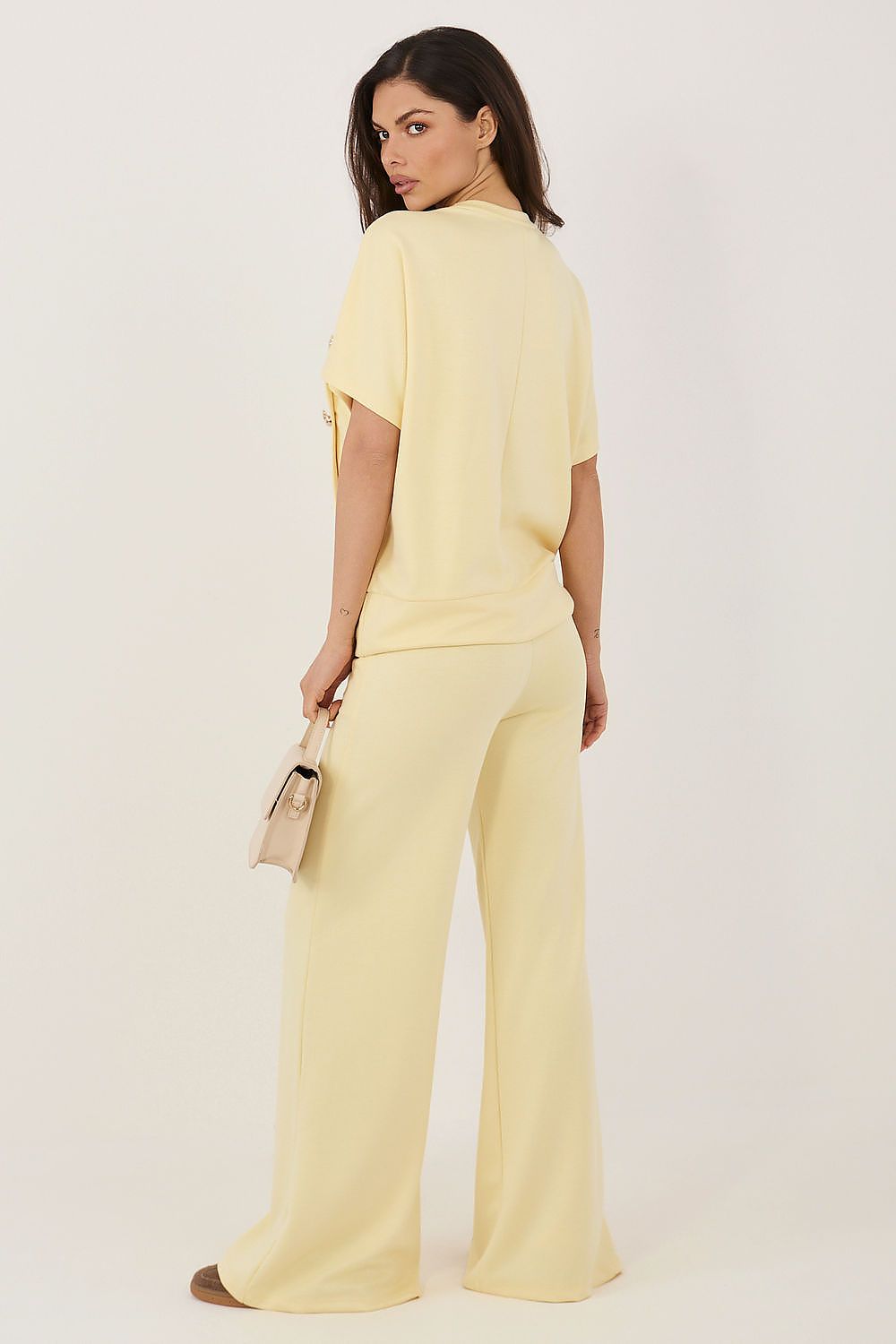 Woman wearing a light yellow outfit with wide-leg pants on a white background