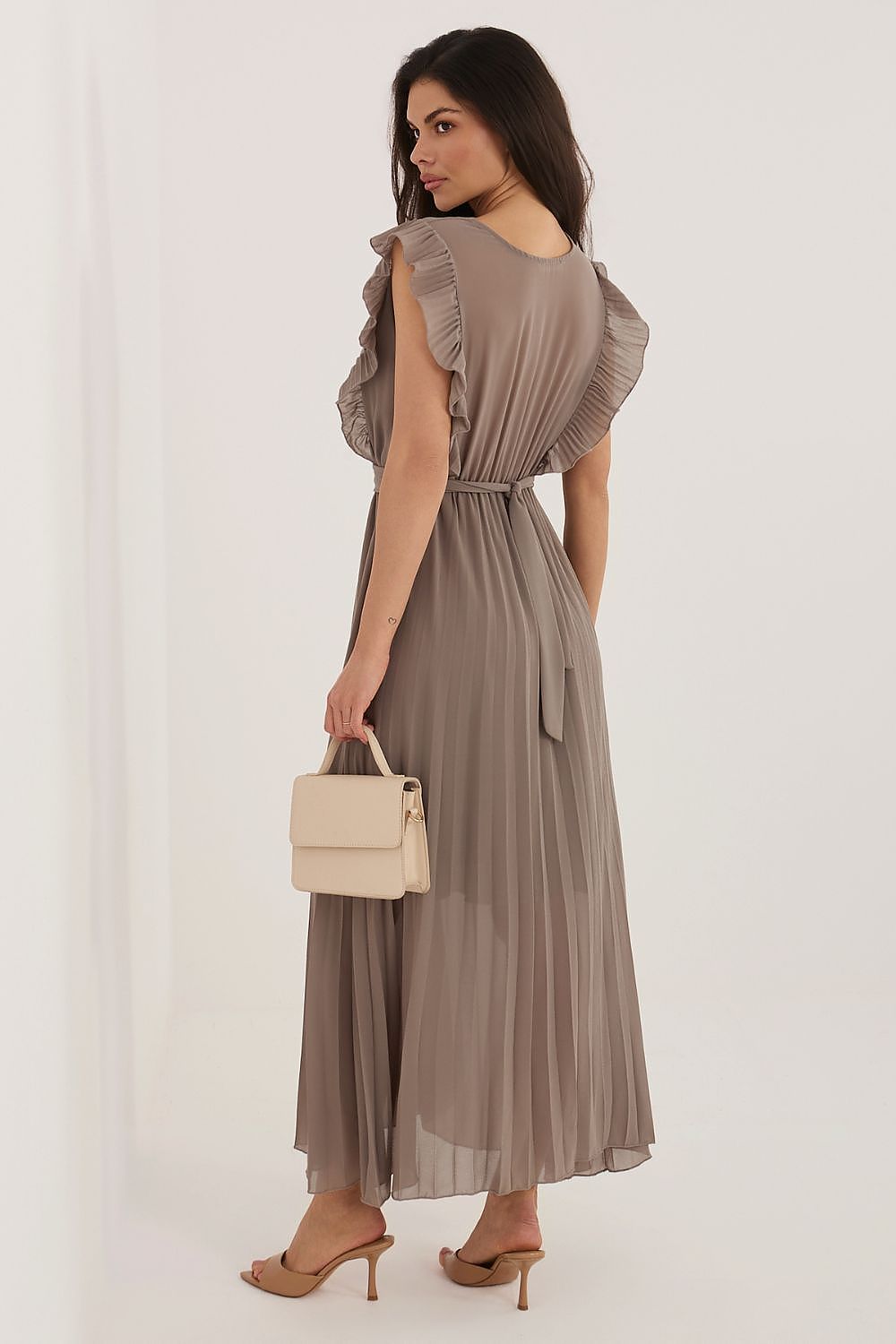 Woman wearing a long, light brown dress holding a beige handbag on a white background